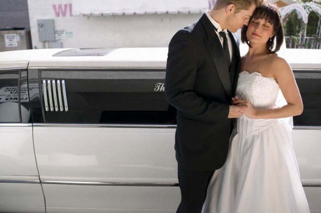 Bride and Groom Standing Together in Front of a Stretch Limousine